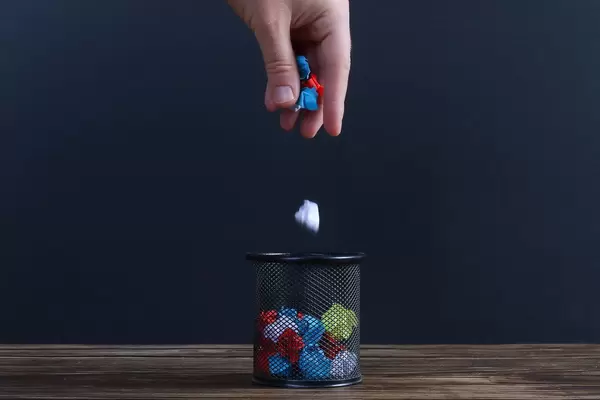 Hand putting crumpled paper into a trash can on black background