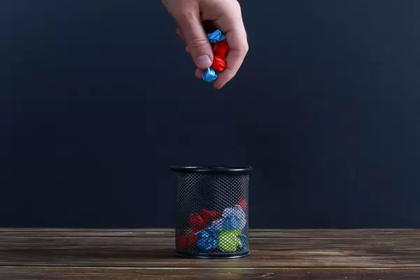 Hand putting crumpled paper into a trash can
