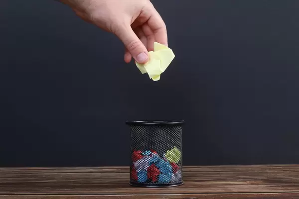 Hand putting crumpled yellow paper into a trash can