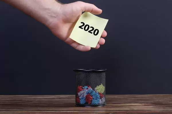 Hand putting paper with 2020 text into a trash can