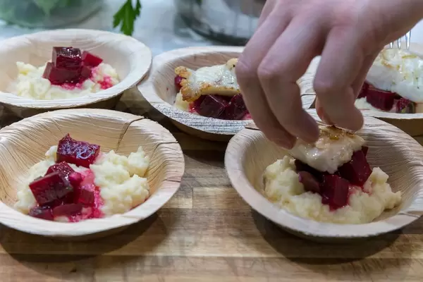 Hand richtet mehrere Teller mit Fischgericht mit roter Bete an