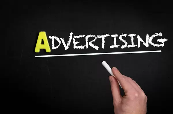 Hand schreibt das Wort "Advertising" - Werbung - auf eine schwarze Tafel