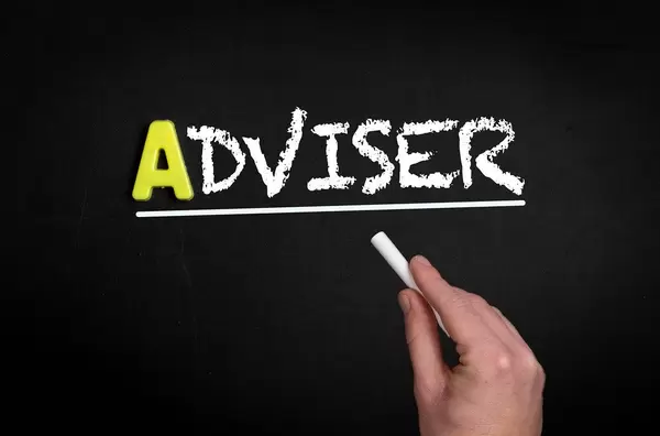 Hand schreibt das Wort "Adviser" - Berater - mit Kreide auf eine schwarze Tafel