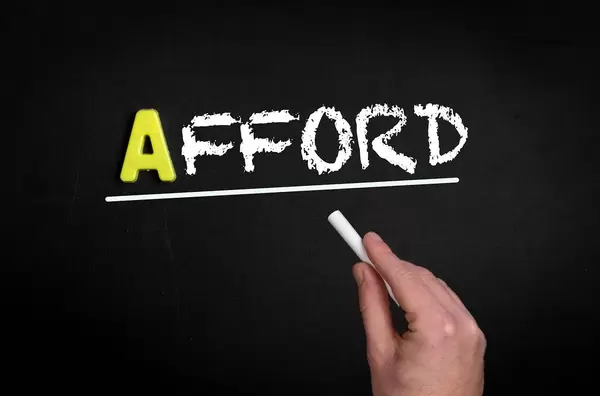 Hand schreibt das Wort "Afford" - sich etwas leisten können - mit Kreide  auf eine schwarze Tafel