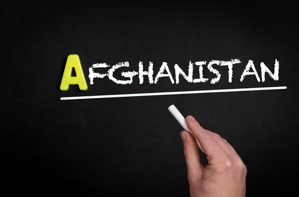 Hand schreibt das Wort "Afghanistan" mit Kreide auf eine schwarze Tafel