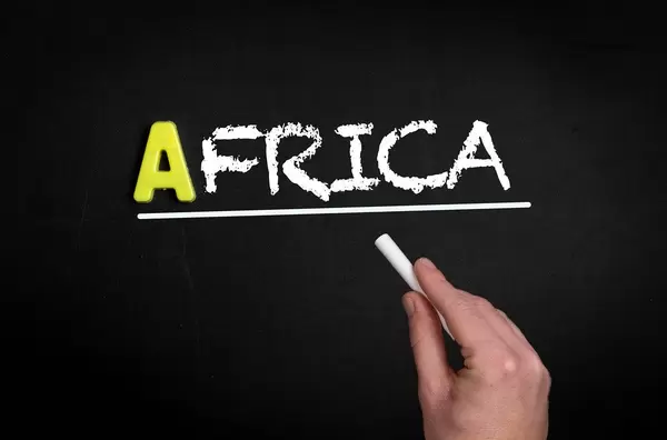 Hand schreibt das Wort "Afrika" mit Kreide auf eine schwarze Tafel