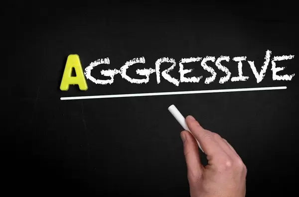 Hand schreibt das Wort "Aggressiv" mit Kreide auf eine schwarze Tafel