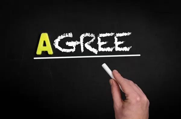 Hand schreibt das Wort "Agree" - Zustimmen - mit Kreide auf eine schwarze Tafel