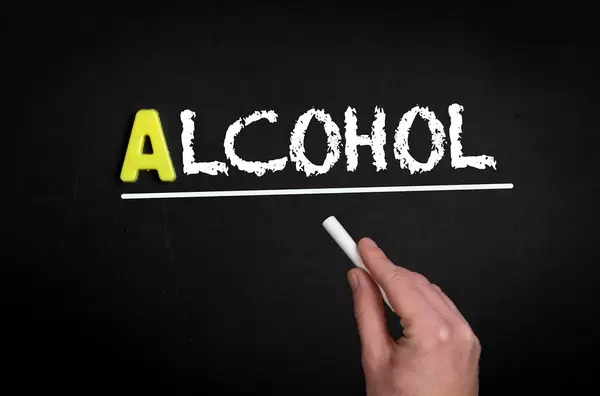 Hand schreibt das Wort "Alkohol" mit Kreide auf eine schwarze Tafel