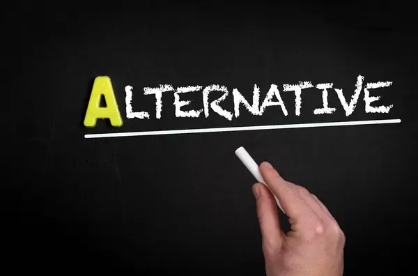 Hand schreibt das Wort "Alternative" mit Kreide auf eine schwarze Tafel