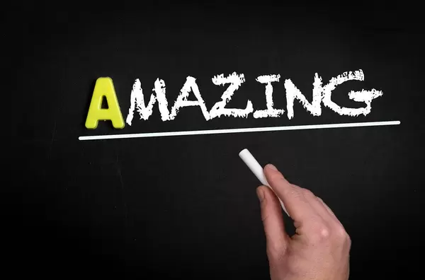 Hand schreibt das Wort "Amazing" - Großartig - mit Kreide auf eine schwarze Tafel