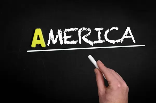 Hand schreibt das Wort "Amerika" mit Kreide auf eine schwarze Tafel
