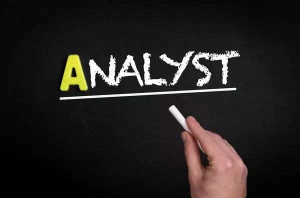 Hand schreibt das Wort "Analyst" mit Kreide auf eine schwarze Tafel