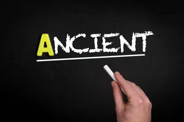 Hand schreibt das Wort "Ancient" - antik / historisch - mit Kreide auf eine schwarze Tafel
