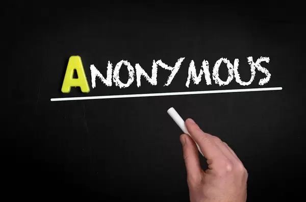 Hand schreibt das Wort "Anonymous" - anonym - mit Kreide auf eine schwarze Tafel