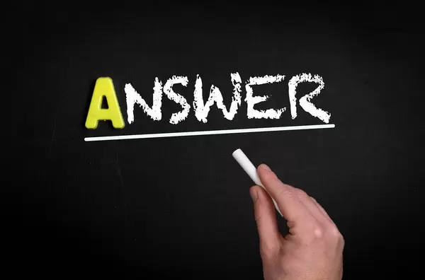 Hand schreibt das Wort "Answer" - Antwort - mit Kreide auf eine schwarze Tafel