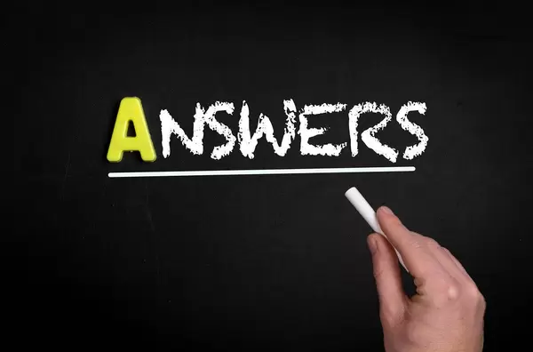 Hand schreibt das Wort "Answers" - Antworten - mit Kreide auf eine schwarze Tafel