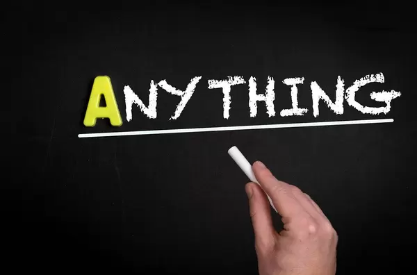 Hand schreibt das Wort "Anything" - Irgendetwas - mit Kreide auf eine schwarze Tafel