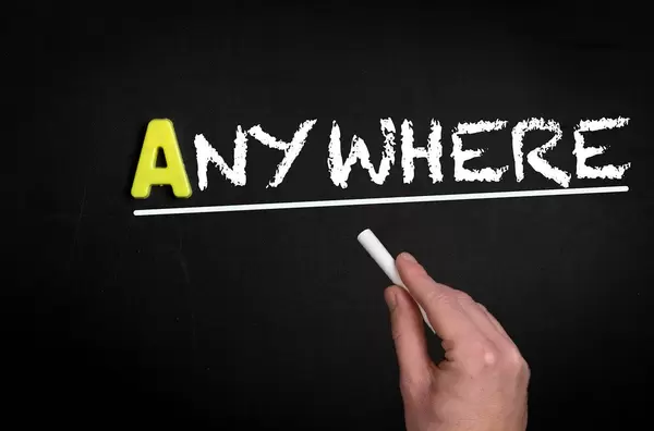 Hand schreibt das Wort "Anywhere" - Irgendwo - mit Kreide auf eine schwarze Tafel