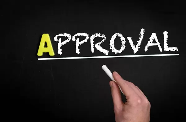 Hand schreibt das Wort "Approval" - Genehmigung - mit Kreide auf eine schwarze Tafel