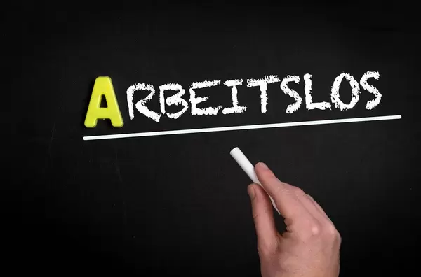 Hand schreibt das Wort "Arbeitslos" mit Kreide auf eine schwarze Tafel