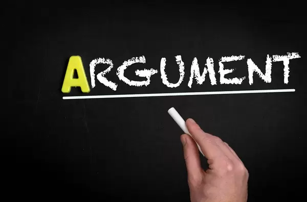 Hand schreibt das Wort "Argument" - Streit - mit Kreide auf eine schwarze Tafel