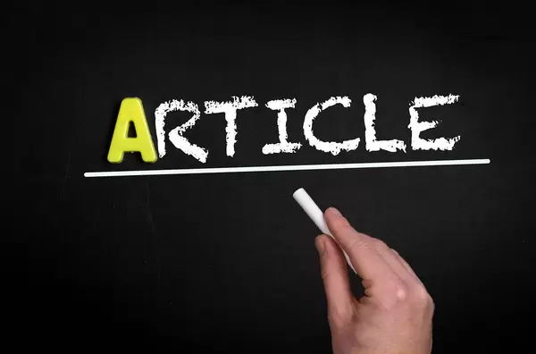 Hand schreibt das Wort "Article" - Artikel - mit Kreide auf eine schwarze Tafel