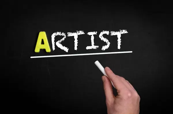 Hand schreibt das Wort "Artist" - Künstler - mit Kreide auf eine schwarze Tafel
