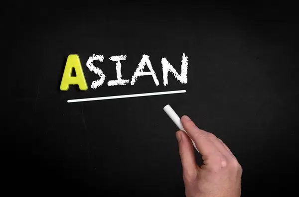 Hand schreibt das Wort "Asian" - Asiatisch - mit Kreide auf eine schwarze Tafel