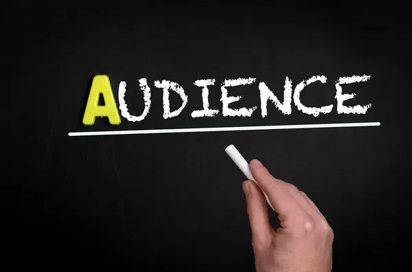 Hand schreibt das Wort "Audience" - Publikum - mit Kreide auf eine schwarze Tafel