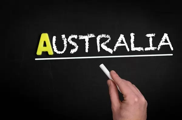 Hand schreibt das Wort "Australien" mit Kreide auf eine schwarze Tafel