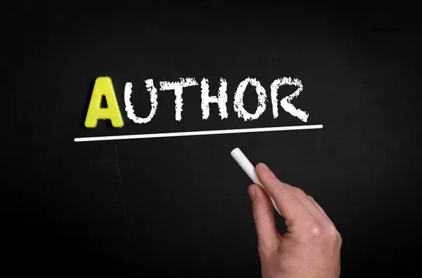 Hand schreibt das Wort "Author" - Autor - mit Kreide auf eine schwarze Tafel