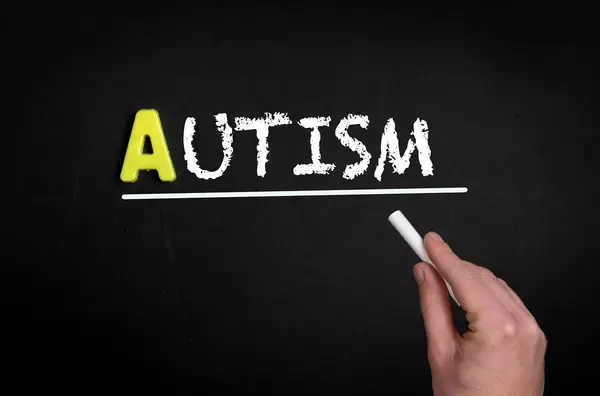 Hand schreibt das Wort "Autism" - Autismus - mit Kreide auf eine schwarze Tafel
