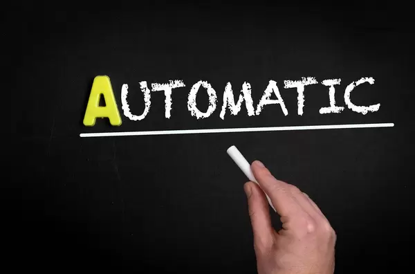 Hand schreibt das Wort "Automatic" - automatisch - mit Kreide auf eine schwarze Tafel