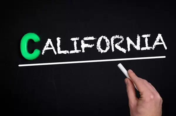 Hand schreibt das Wort "California" - Kalifornien - mit Kreide auf eine schwarze Tafel