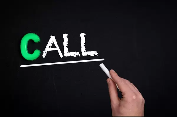 Hand schreibt das Wort "Call" - Anrufen / Gespräch - mit Kreide auf eine schwarze Tafel