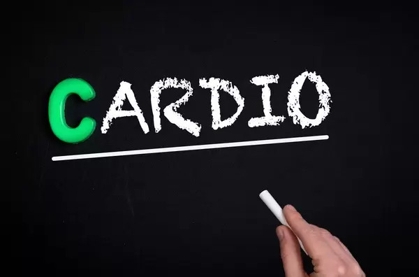 Hand schreibt das Wort "Cardio" mit Kreide auf eine schwarze Tafel