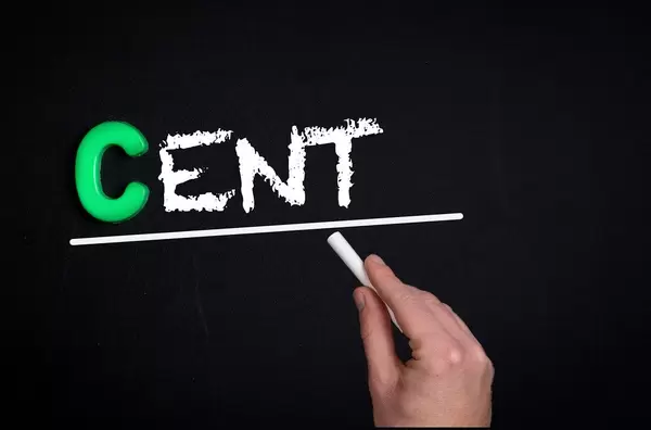 Hand schreibt das Wort "Cent" mit Kreide auf eine schwarze Tafel