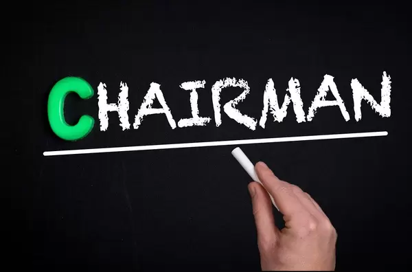 Hand schreibt das Wort "Chairman" - Vorsitzender - mit Kreide auf eine schwarze Tafel