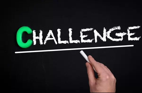 Hand schreibt das Wort "Challenge" - Herausforderung - mit Kreide auf eine schwarze Tafel