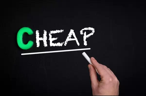 Hand schreibt das Wort "Cheap" - Billig - mit Kreide auf eine schwarze Tafel