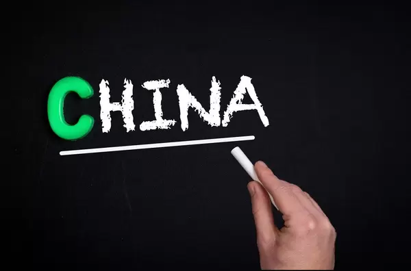 Hand schreibt das Wort "China" mit Kreide auf eine schwarze Tafel