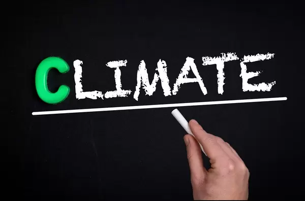 Hand schreibt das Wort "Climate" - Klima - mit Kreide auf eine schwarze Tafel