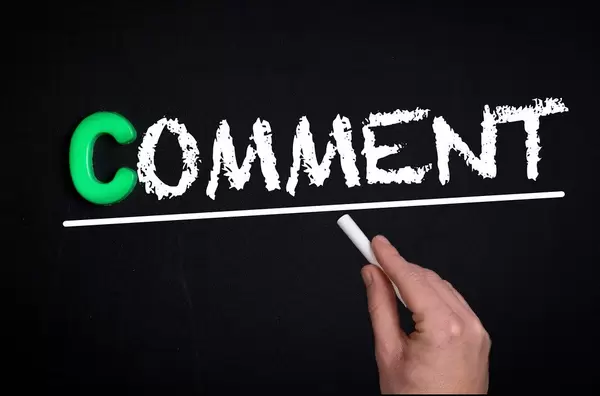Hand schreibt das Wort "Comment" - Kommentar - mit Kreide auf eine schwarze Tafel