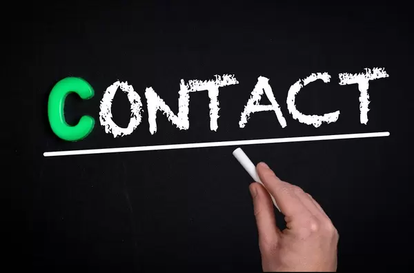 Hand schreibt das Wort "Contact" - Kontakt - mit Kreide auf eine schwarze Tafel