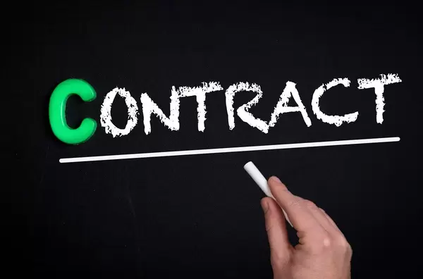 Hand schreibt das Wort "Contract" - Vertrag - mit Kreide auf eine schwarze Tafel