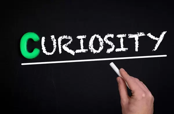 Hand schreibt das Wort "Couriosity" - Neugierde - mit Kreide auf eine schwarze Tafel