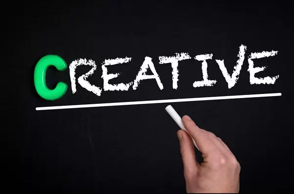 Hand schreibt das Wort "Creative" - Kreativ - mit Kreide auf eine schwarze Tafel