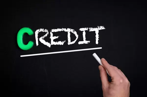 Hand schreibt das Wort "Credit" - Kredit - mit Kreide auf eine schwarze Tafel