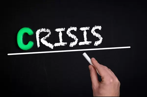 Hand schreibt das Wort "Crisis" - Krise - mit Kreide auf eine schwarze Tafel